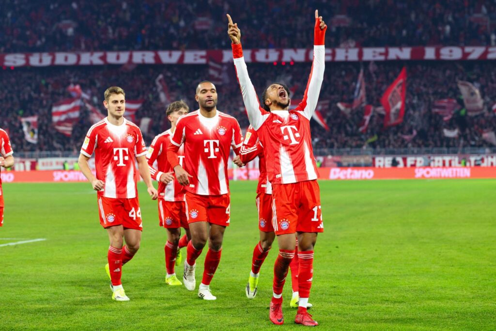 Bayern München Fußballspieler jubeln auf dem Spielfeld beim Match, gekleidet in roten Trikots mit weißen Streifen, fröhliche Atmosphäre, aktuelle Bundesliga News, Fokus auf FC Bayern Erfolg.
